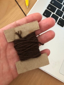 Dark brown yarn wound round a small cardboard bobbin